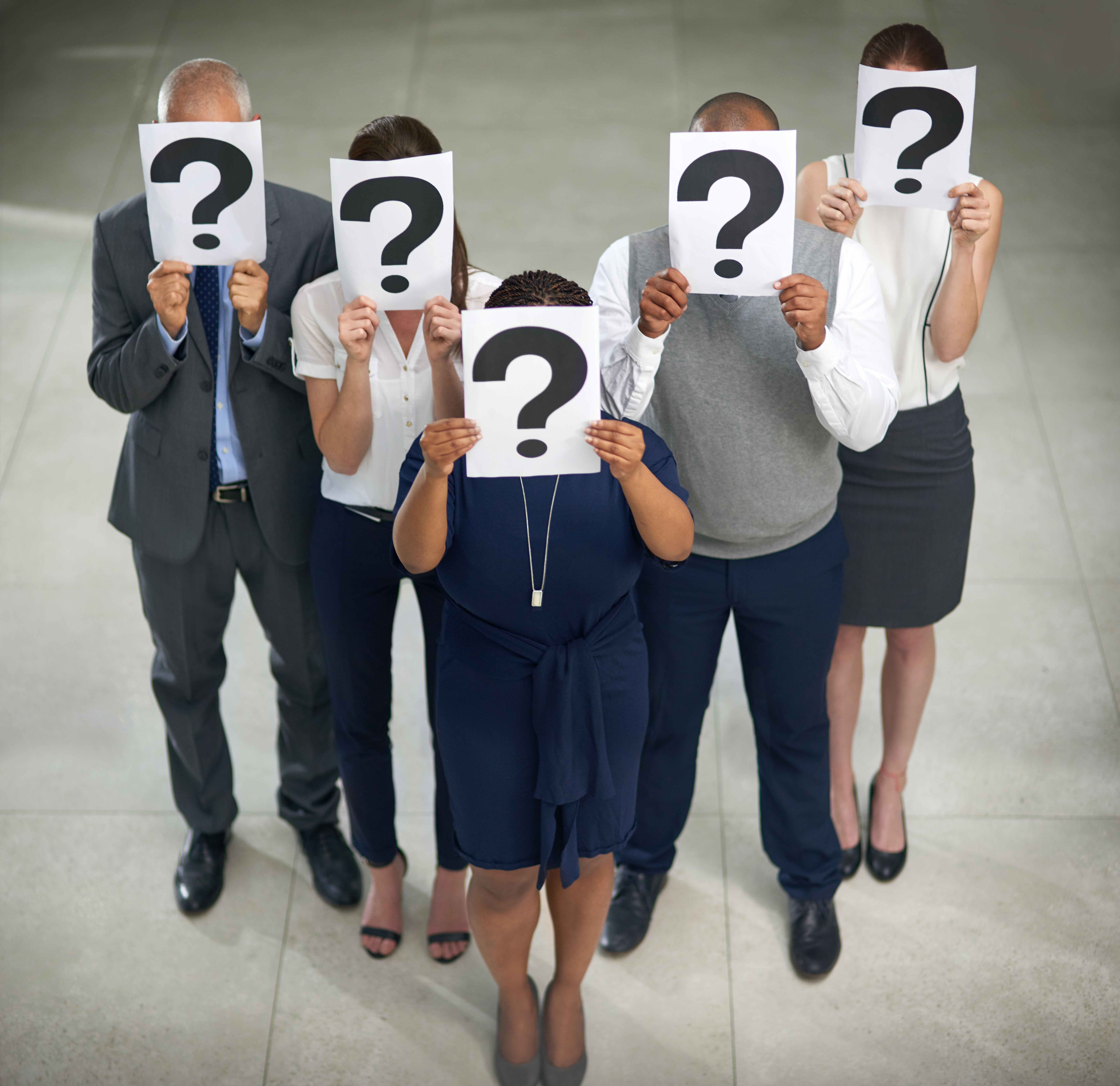 High angle shot of a group of businesspeople holding questions marks in front of their faces.